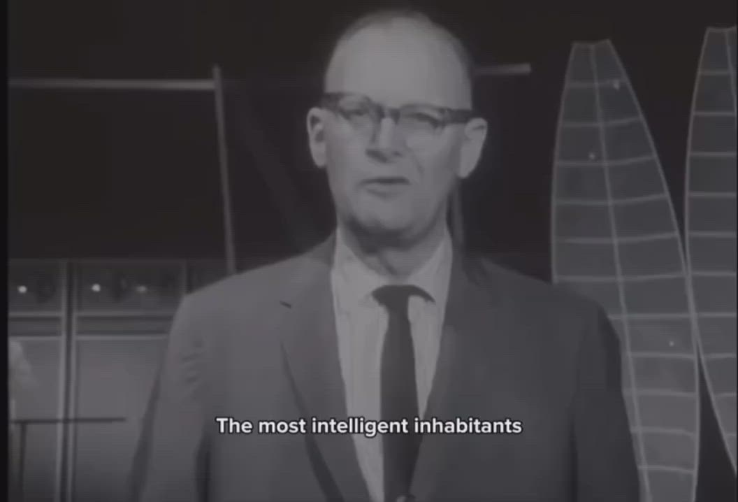 Black-and-white video frame of a man in glasses speaking; subtitle reads 'The most intelligent inhabitants'
